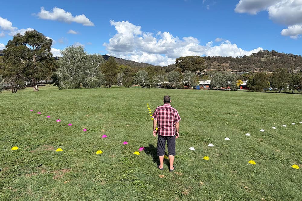 Person standing in front of three coloured cone paths on grass, representing Orientation and Mobility training for people with brain‑based vision impairment.